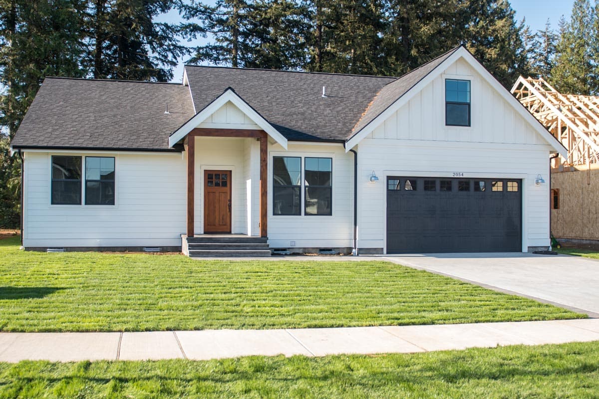 House plan exterior: Modern Farmhouse style, one story, white siding, wood front door, dark garage door, gabled dormer over garage.