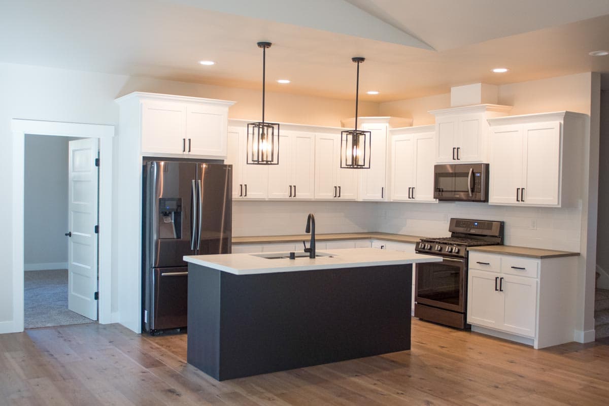 Kitchen with white cabinets, stainless steel appliances, dark island with sink, and pendant lighting.