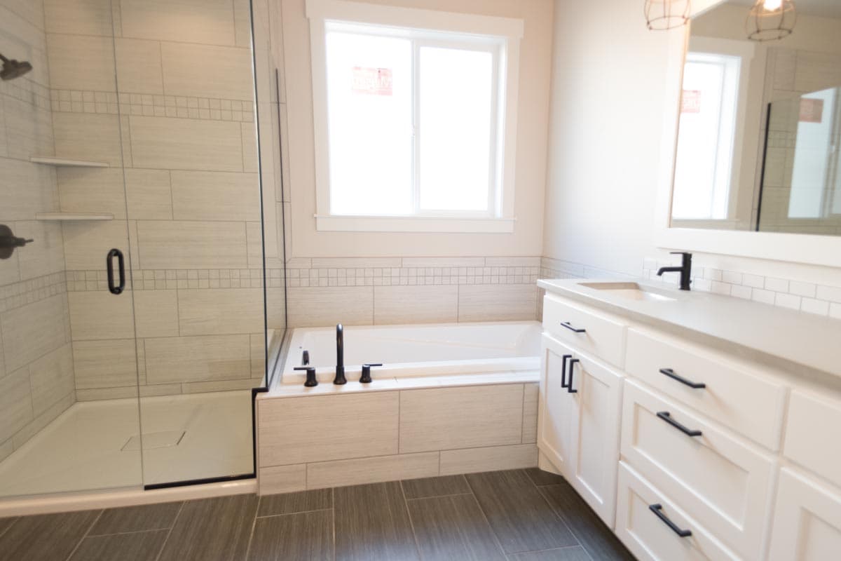Modern bathroom with freestanding tub, glass-enclosed shower, and double vanity with white cabinetry and dark hardware.