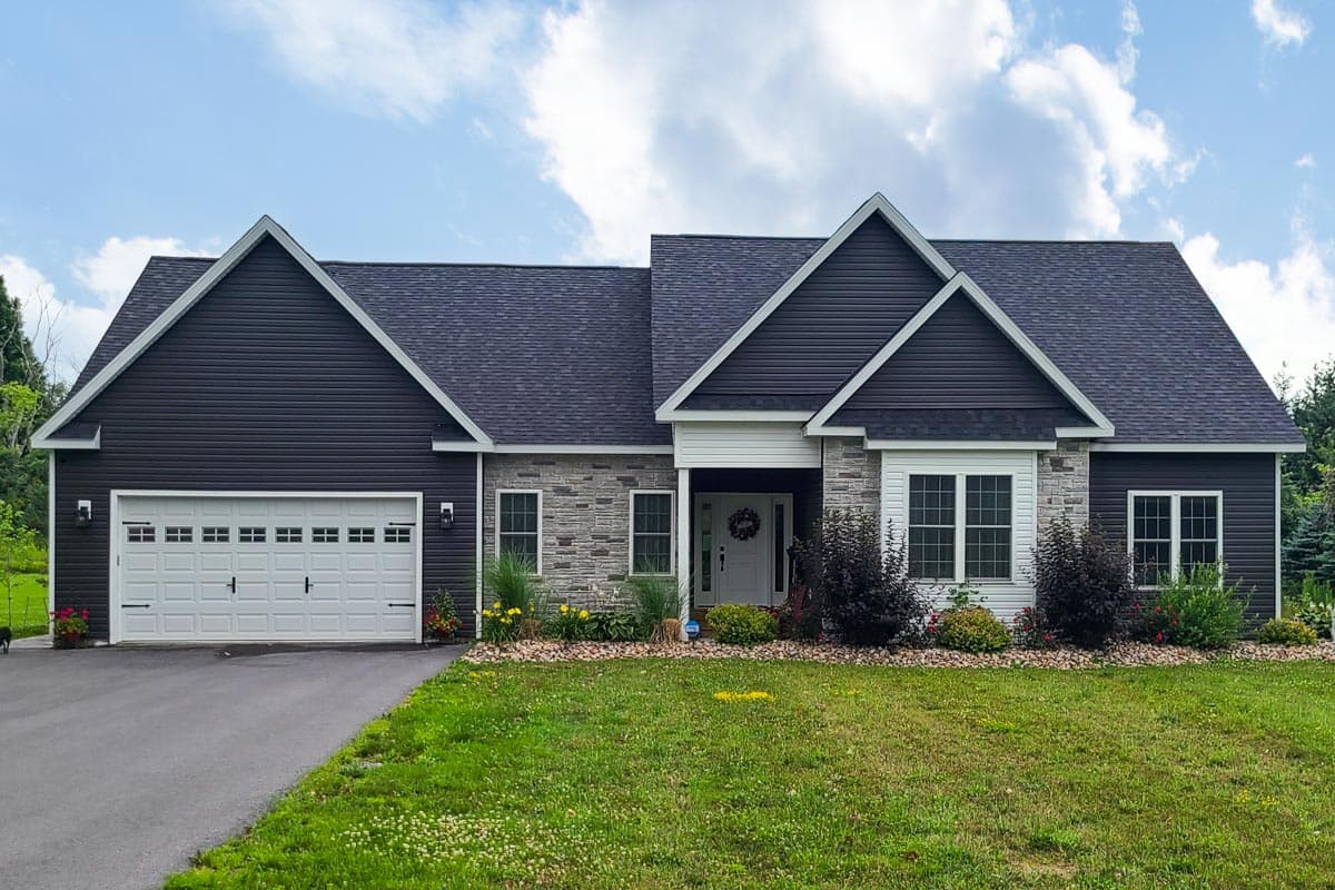 House plan exterior: single-story Modern Farmhouse with dark vinyl siding, stone accents, prominent gables, and a two-car garage.