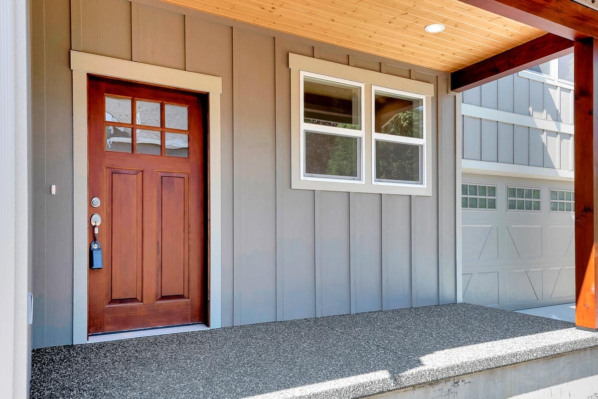 House plan exterior with wooden front door, adjacent window, and garage doors. Modern Farmhouse style.