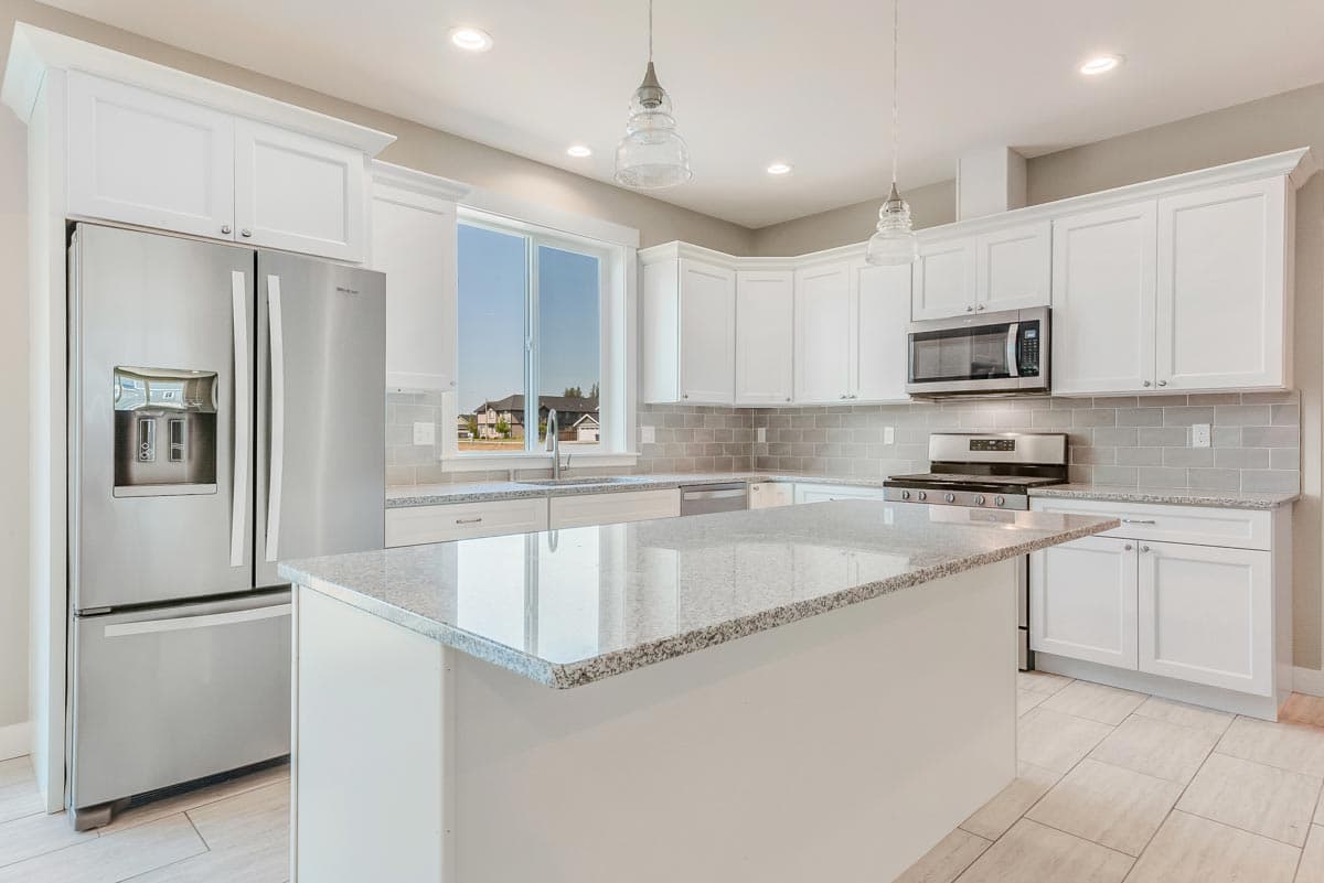 Kitchen with white cabinets, granite countertops, large island, stainless steel appliances, and subway tile backsplash.