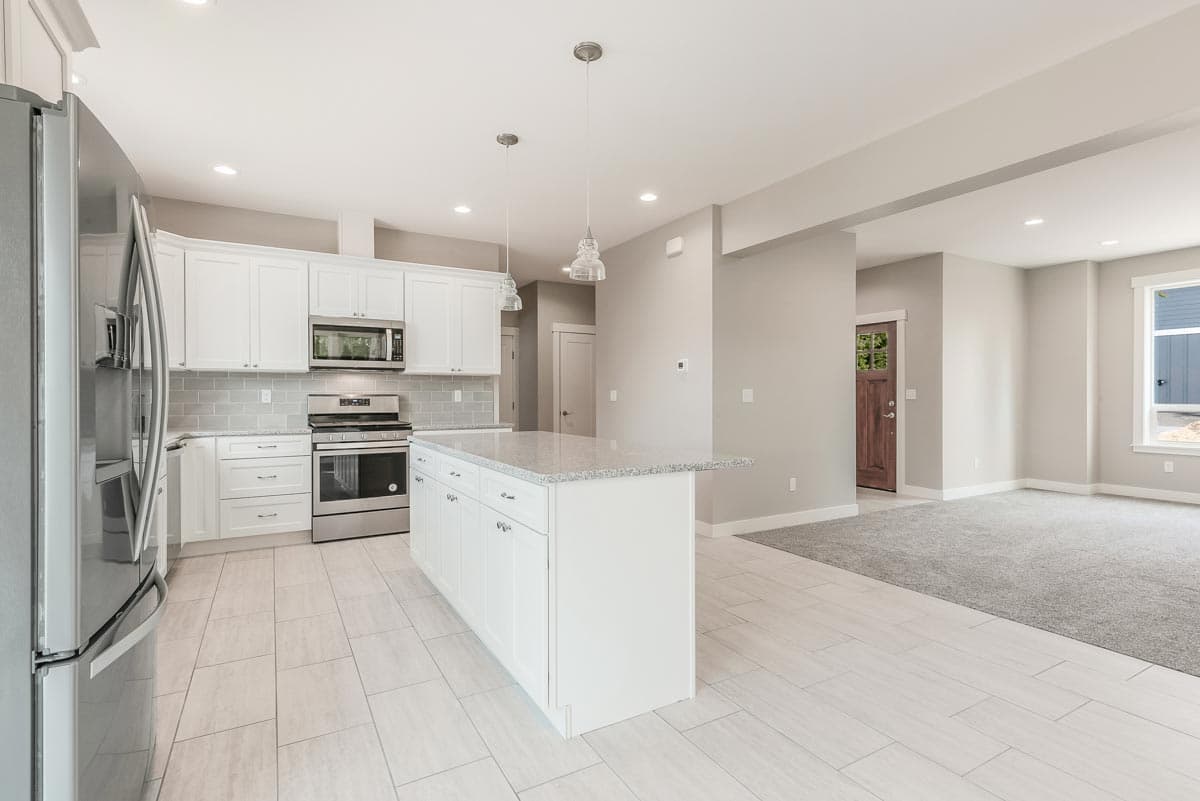 Modern kitchen with white cabinets, granite island, stainless steel appliances, and open concept to living area.