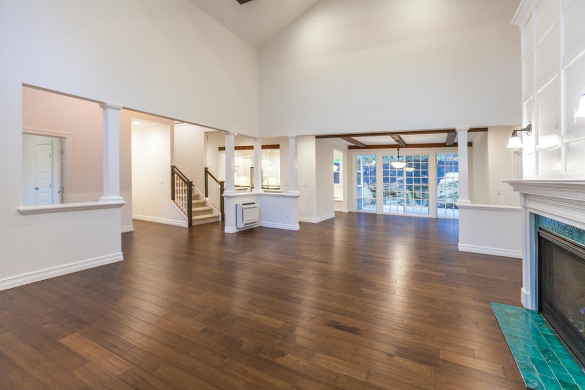 Interior view of a great room with vaulted ceilings, exposed beams, fireplace, and glass doors leading outdoors.