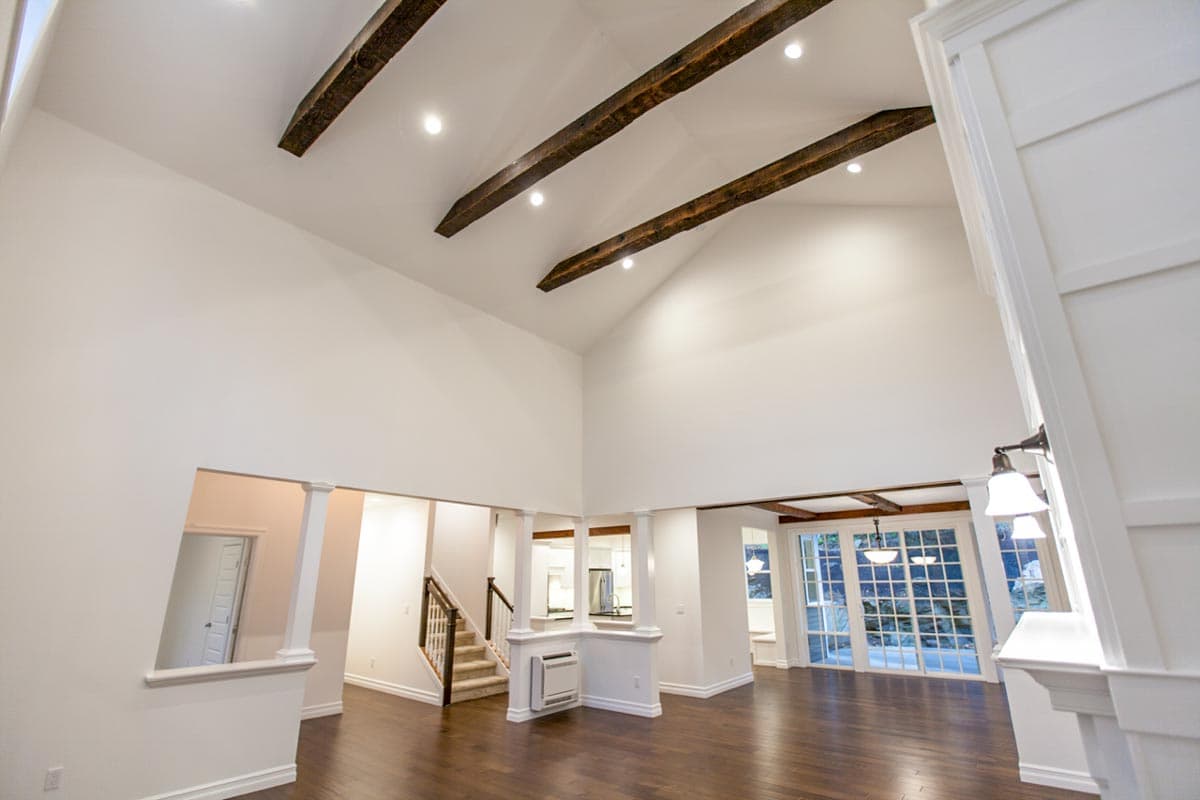 Interior view of a house plan featuring a great room with vaulted ceilings, exposed wooden beams, and a large glass door.