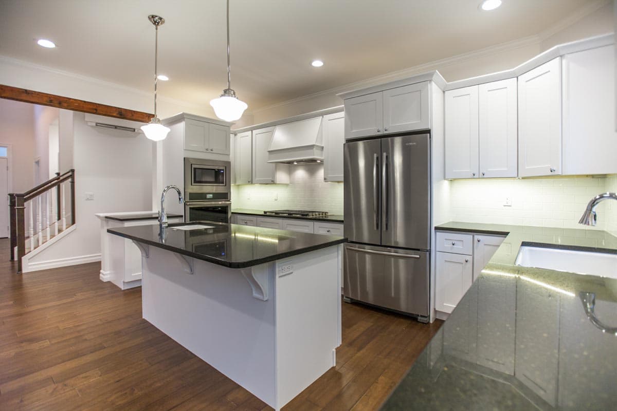 Modern kitchen with large island, stainless steel appliances including refrigerator and microwave, white subway tile backsplash, and wood flooring.