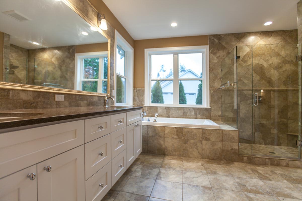 Bathroom with double vanity, soaking tub, and glass-enclosed shower with tile surround.