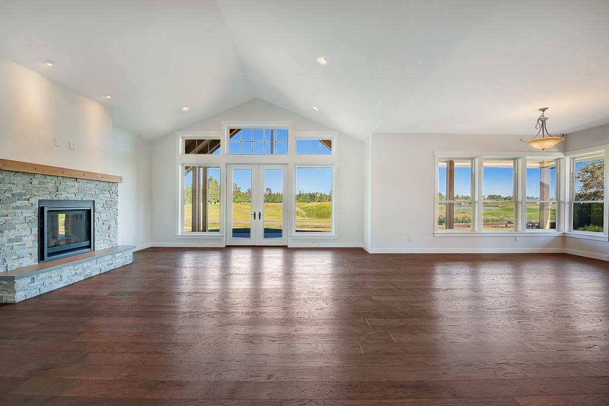 Interior view of a great room with vaulted ceiling, stone fireplace, and large windows overlooking a field.