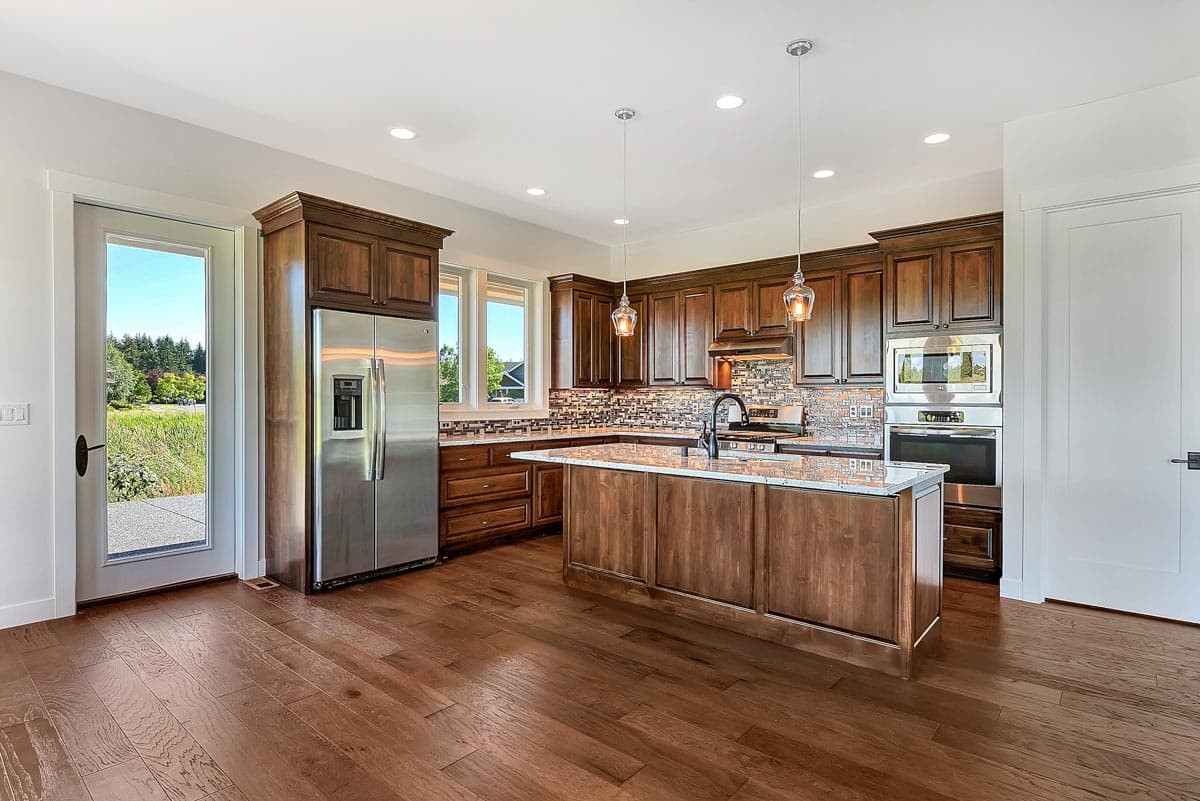 Kitchen with dark wood cabinets, granite countertops, large island with sink, stainless steel appliances, and access to outdoors.