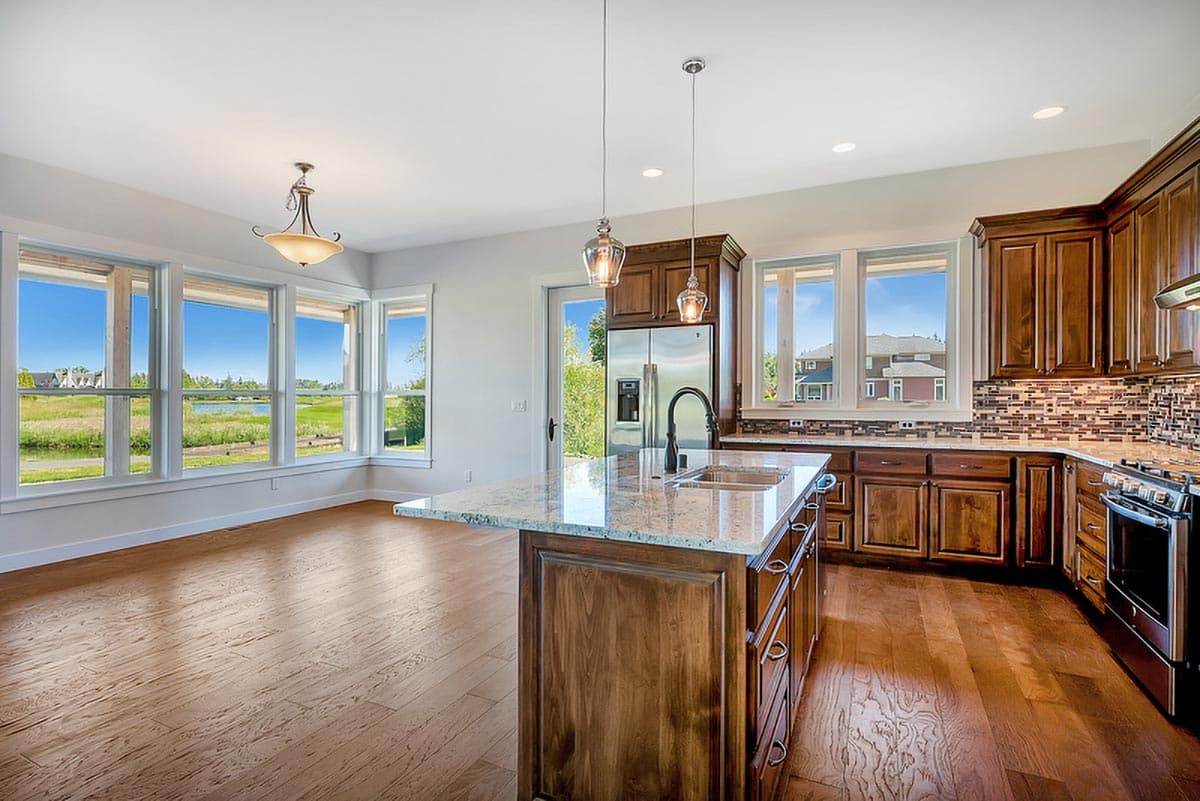 Kitchen with large island, granite countertops, wood cabinets, backsplash, stainless steel appliances, and scenic view windows.