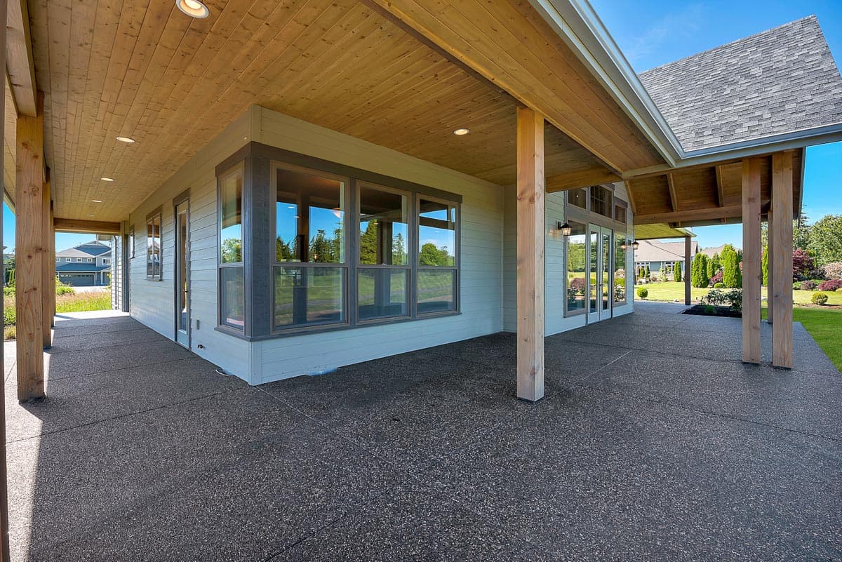 House plan exterior with covered patio, wood ceiling, corner window array, and glass doors.