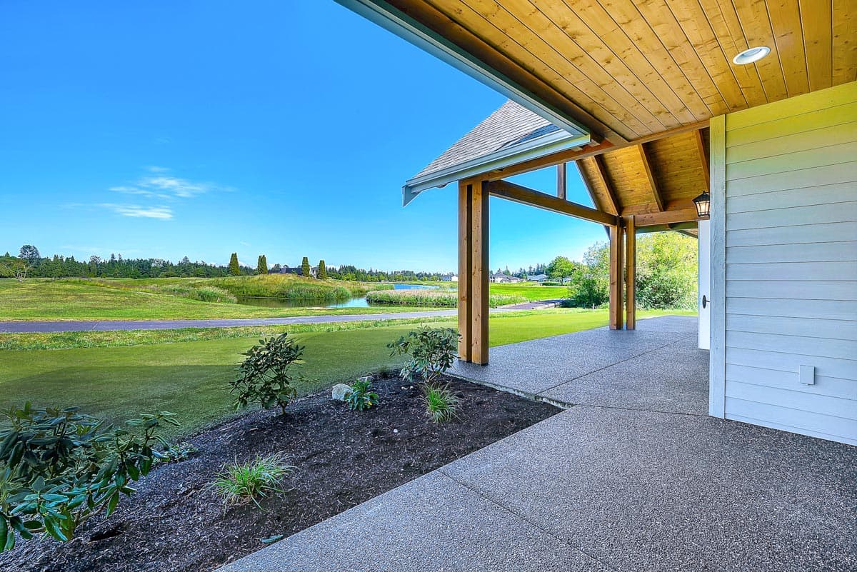 Covered patio with exposed wooden beams and ceiling, overlooking a golf course and pond. House exterior detail.