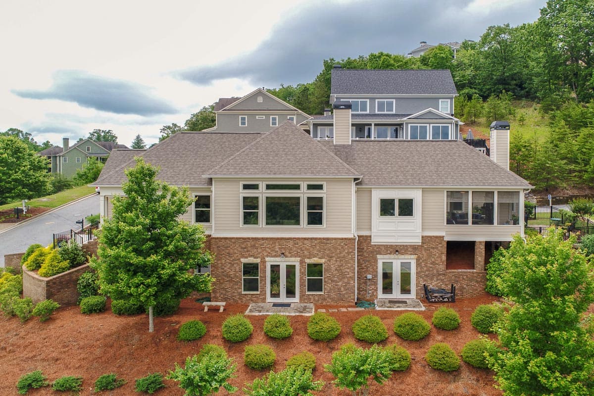 House plan exterior showing a two-story home with brick and siding, large windows, double doors, and a screened porch.