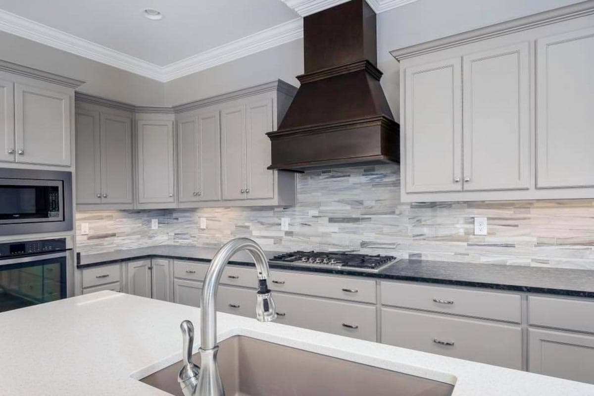 Kitchen with gray cabinets, dark stone countertops, stainless steel sink, gas range, and dark vent hood.