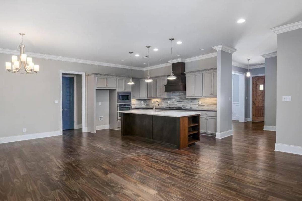 Open-concept kitchen with island, gray cabinetry, stainless steel appliances, and dark wood flooring.
