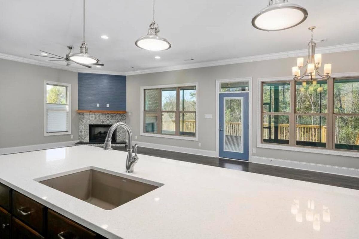 Kitchen and great room with fireplace, sink island, large windows, and blue door leading to deck.
