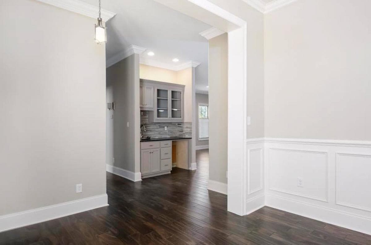 Interior view of a house plan showing a wet bar with gray cabinetry, glass-front upper cabinets, and dark wood flooring.
