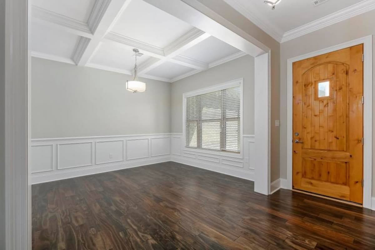 Interior view: Dining room with coffered ceiling, wainscoting, large window, and natural wood door.