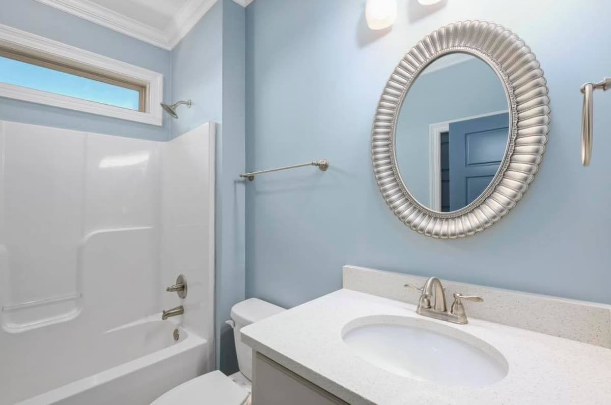Bathroom with bathtub, toilet, vanity with sink, large oval mirror, and horizontal window above tub.