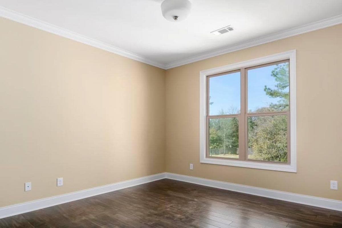 Interior view of an empty room with beige walls, dark wood floor, white trim, and a large double-hung window.