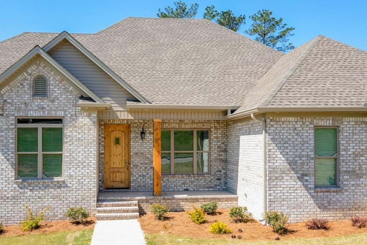 House plan exterior with white brick, wood door, covered porch with wood post, and gabled roof.