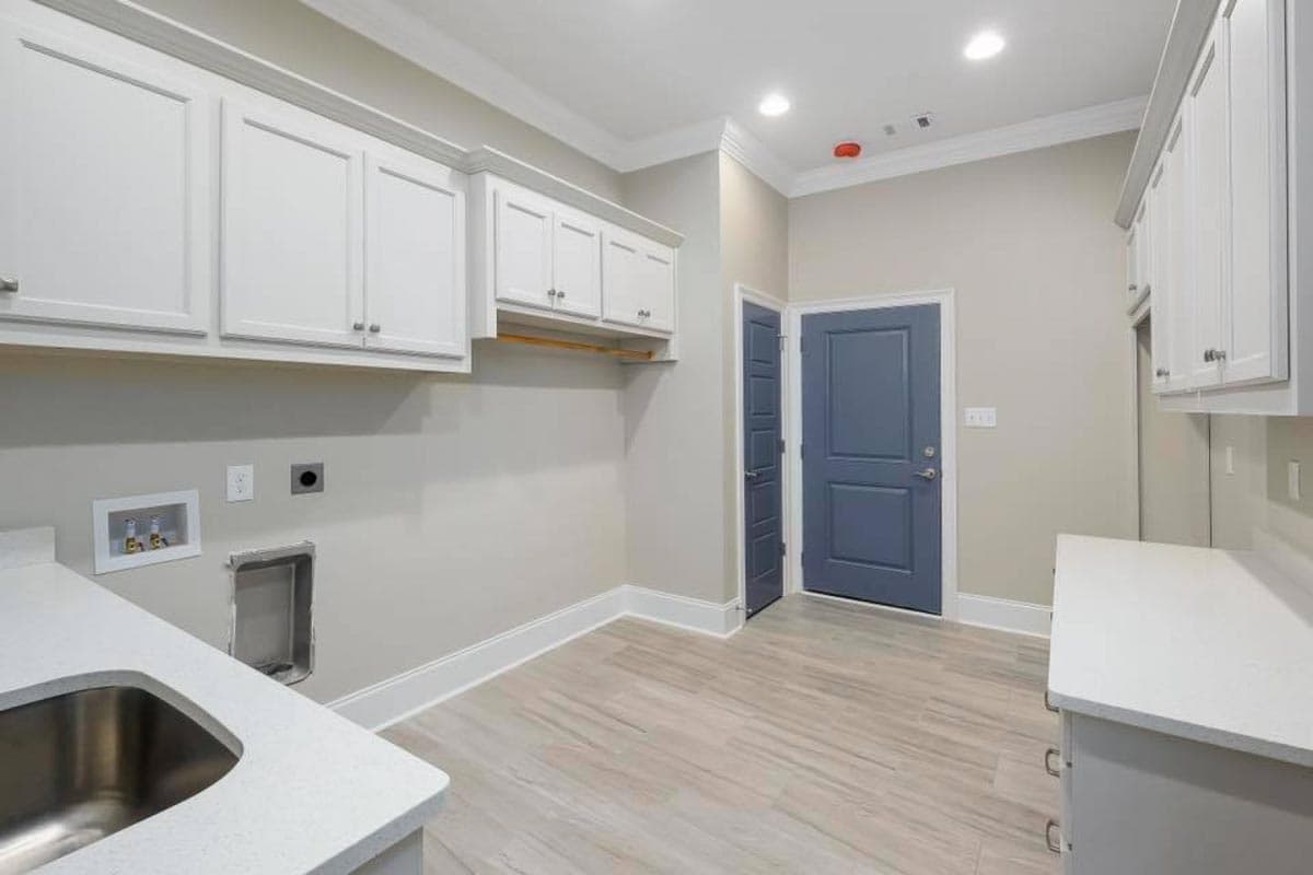 Laundry room with white cabinets, quartz countertops, stainless steel sink, and blue paneled door.
