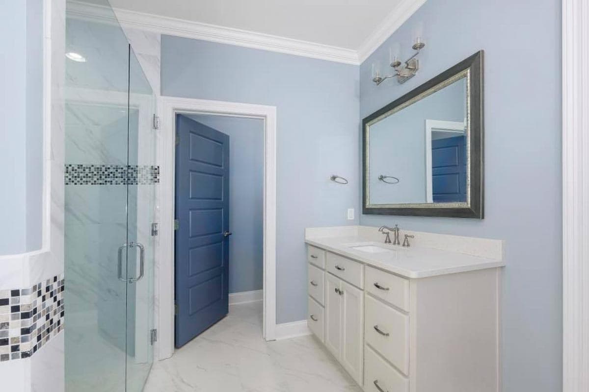 Modern bathroom interior with glass shower, white vanity, marble tile, and blue door.