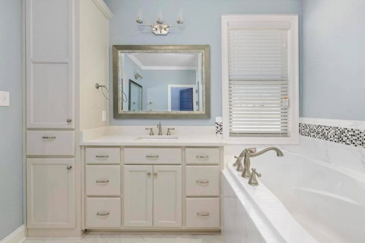 Bathroom vanity with white cabinets, white countertop, and large framed mirror above sink. Freestanding soaking tub to the right.