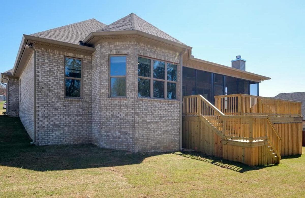 House plan exterior shows brick construction, multi-story rooflines, multiple windows, a screened porch, and a large wooden deck with stairs.