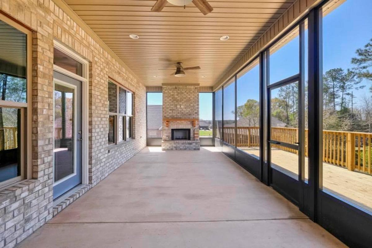 Screened porch with brick fireplace, ceiling fans, and wood deck with railings. House plan exterior.