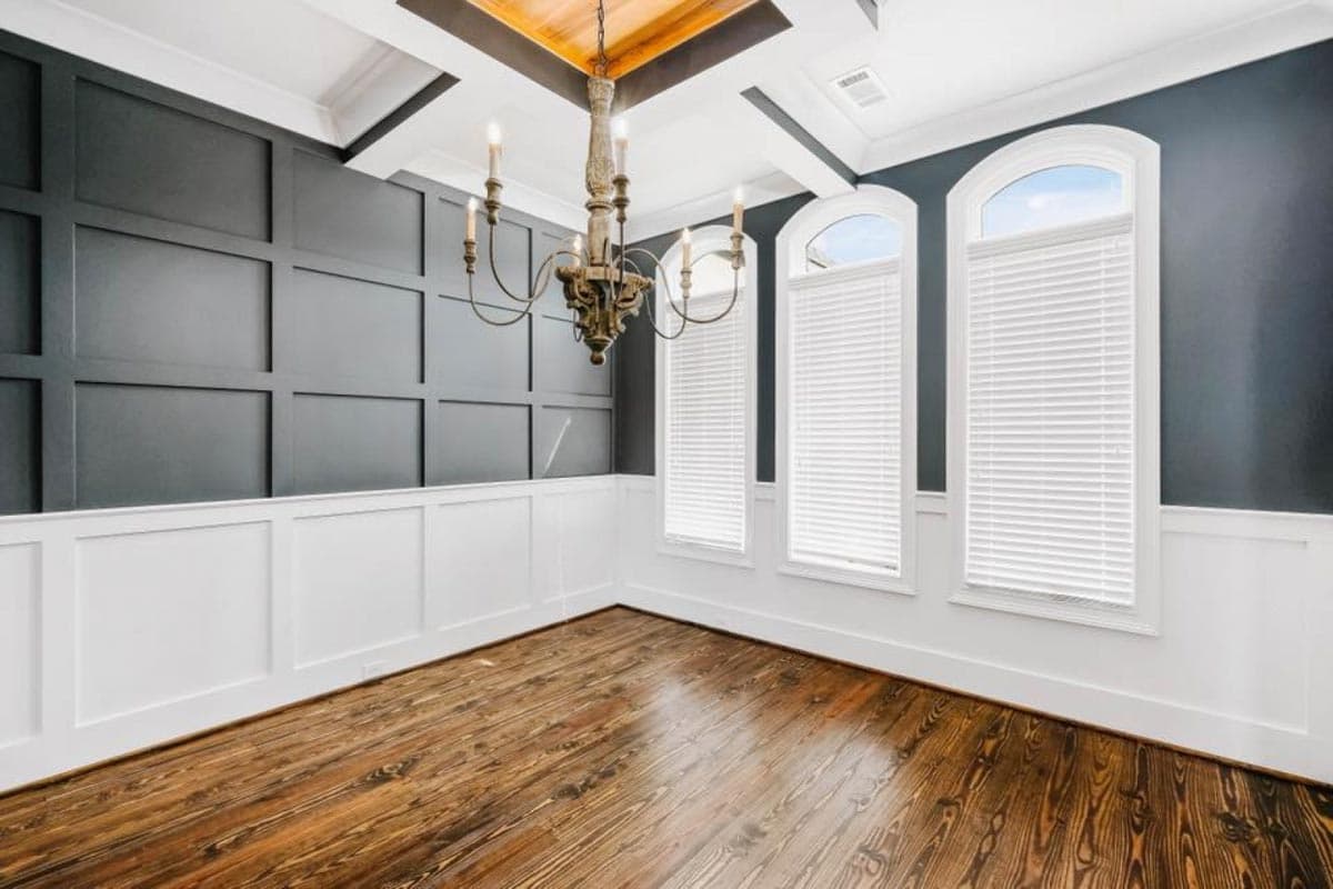 Dining room with wainscoting, coffered ceiling, arched windows, and chandelier.