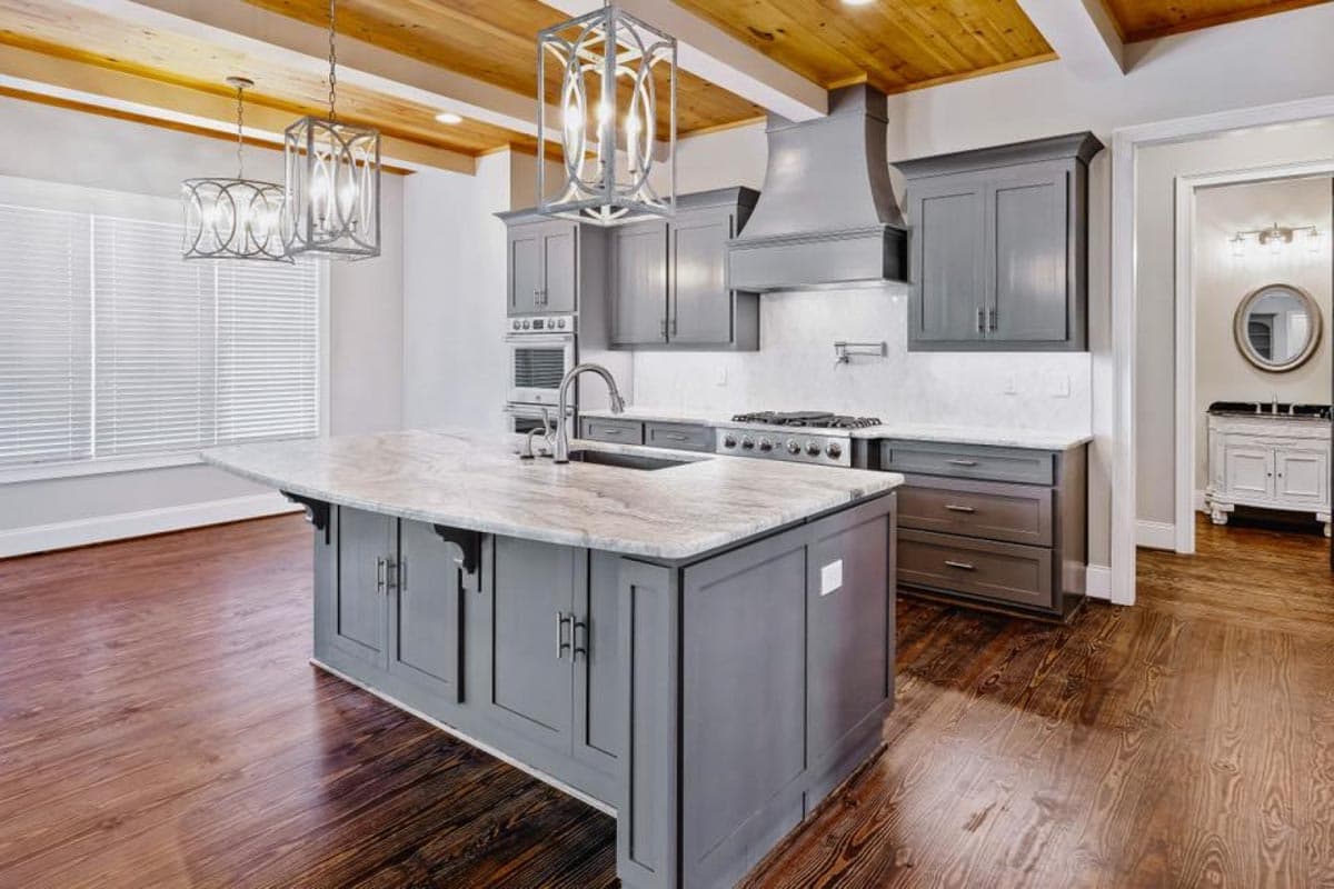 Kitchen with large island, gray cabinetry, marble countertops, stainless steel appliances, and wood-beamed ceiling.
