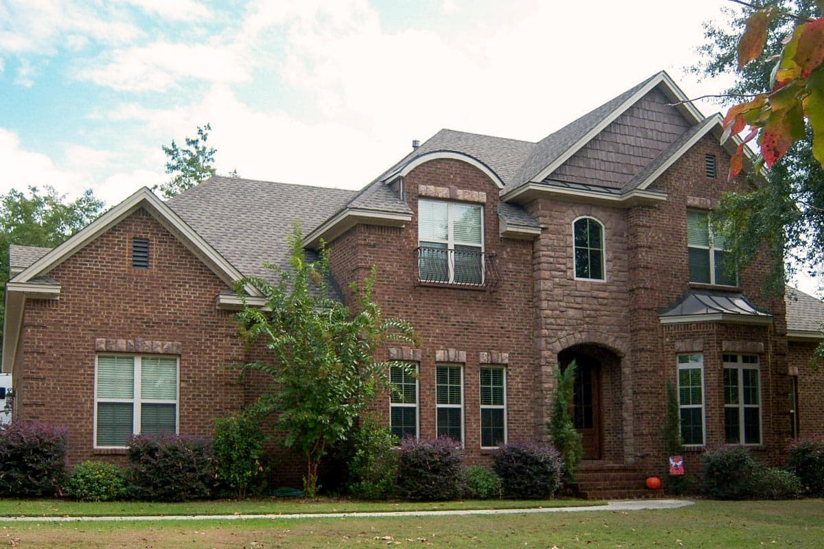 House plan exterior: Brick two-story home with stone accents, arched entry, multiple gables, and a dormer.