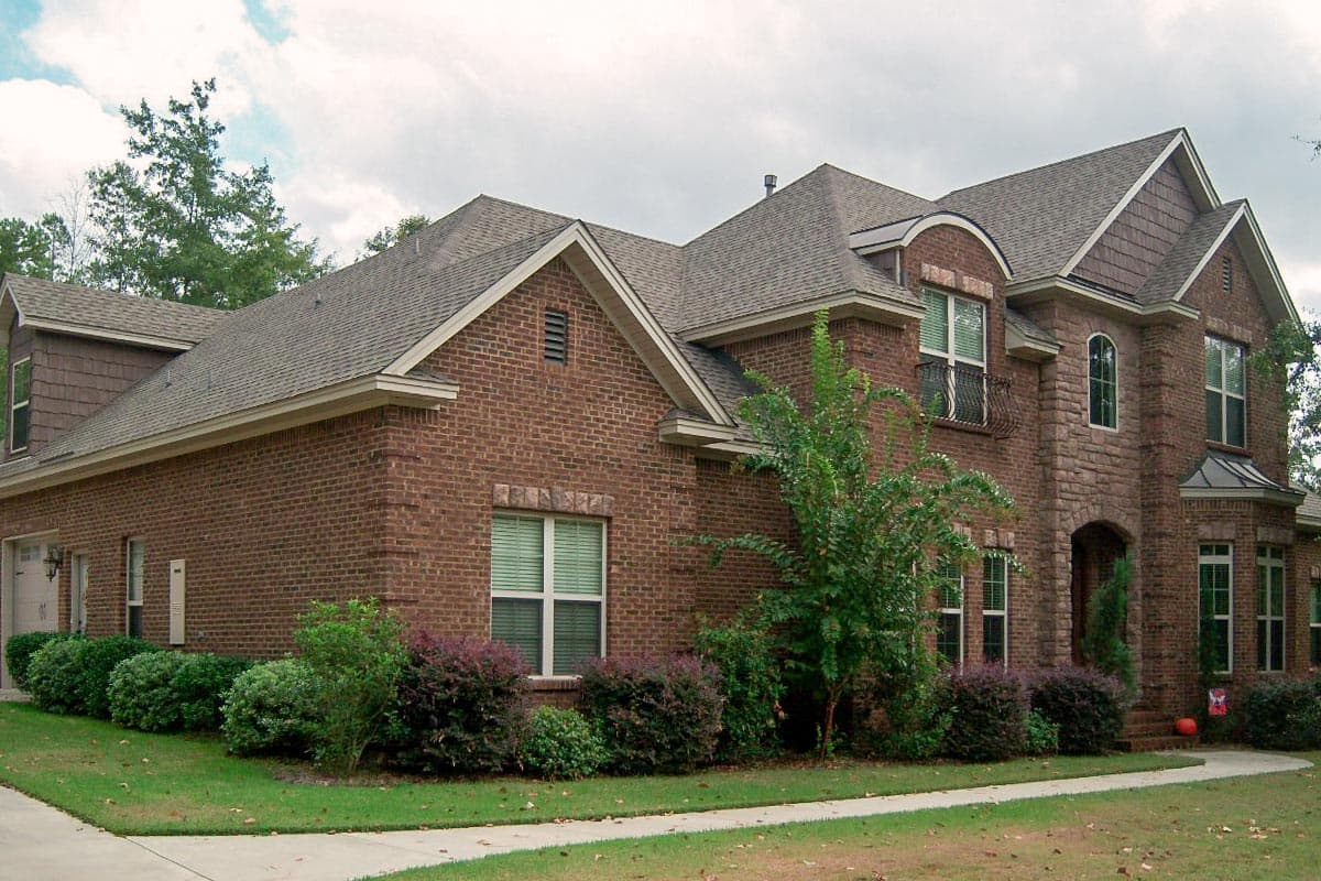 House plan exterior featuring a two-story brick home. Highlights include multiple gables, arched entry, stone facade accent, and dormer windows.