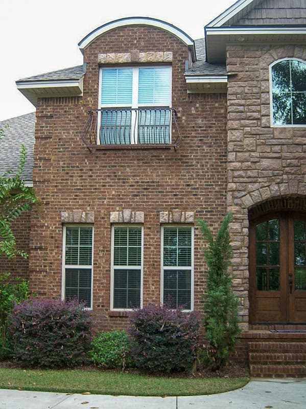 House plan exterior with brick facade, arched entryway, multiple windows, and a decorative balcony.