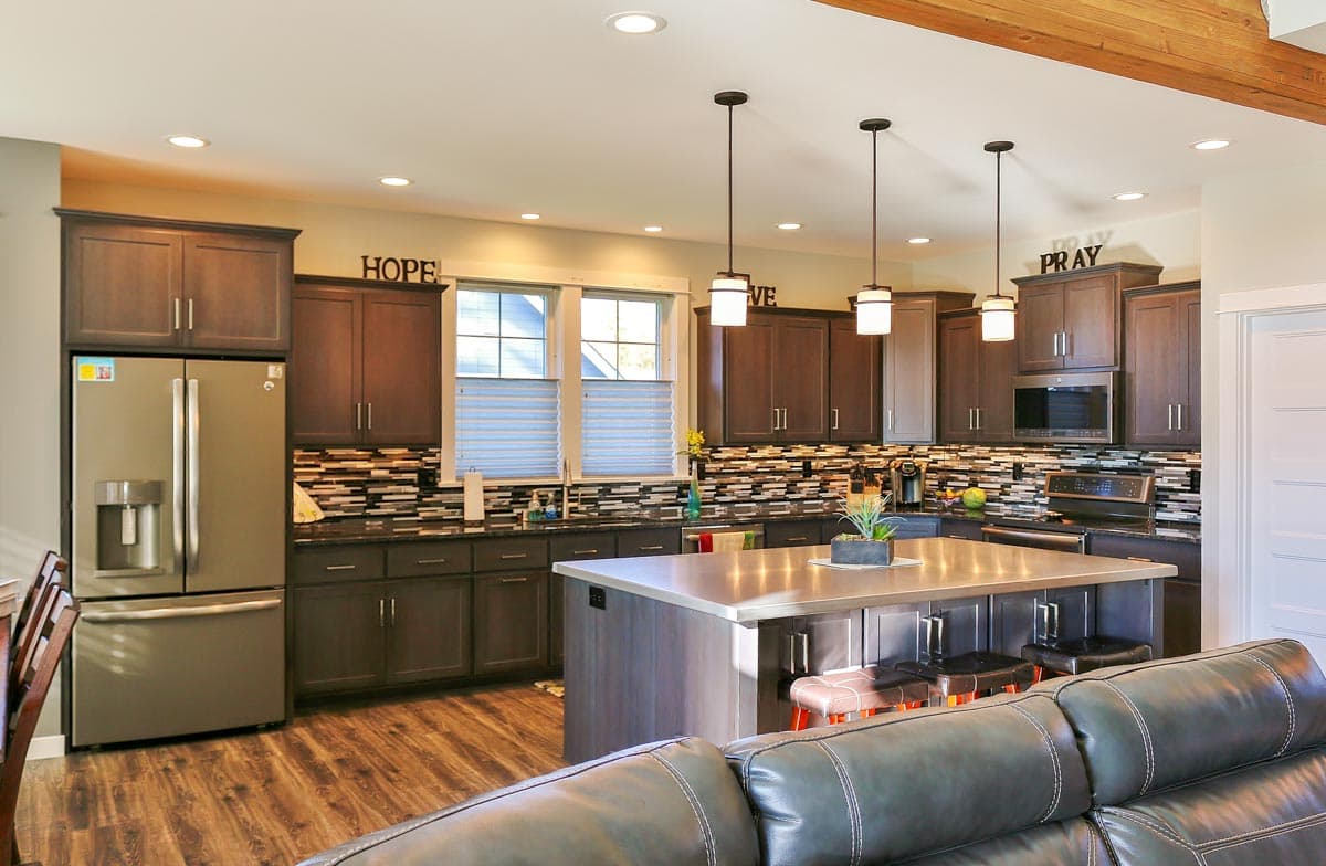 Kitchen interior with dark wood cabinets, stainless steel refrigerator, island with seating, and pendant lights.