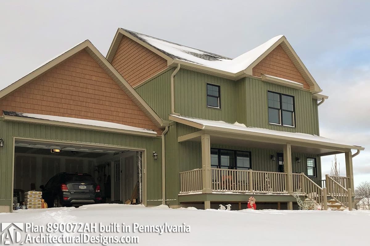 House plan exterior with green siding, front-facing garage, and covered porch with railings. Two stories, prominent gables with cedar shingles.