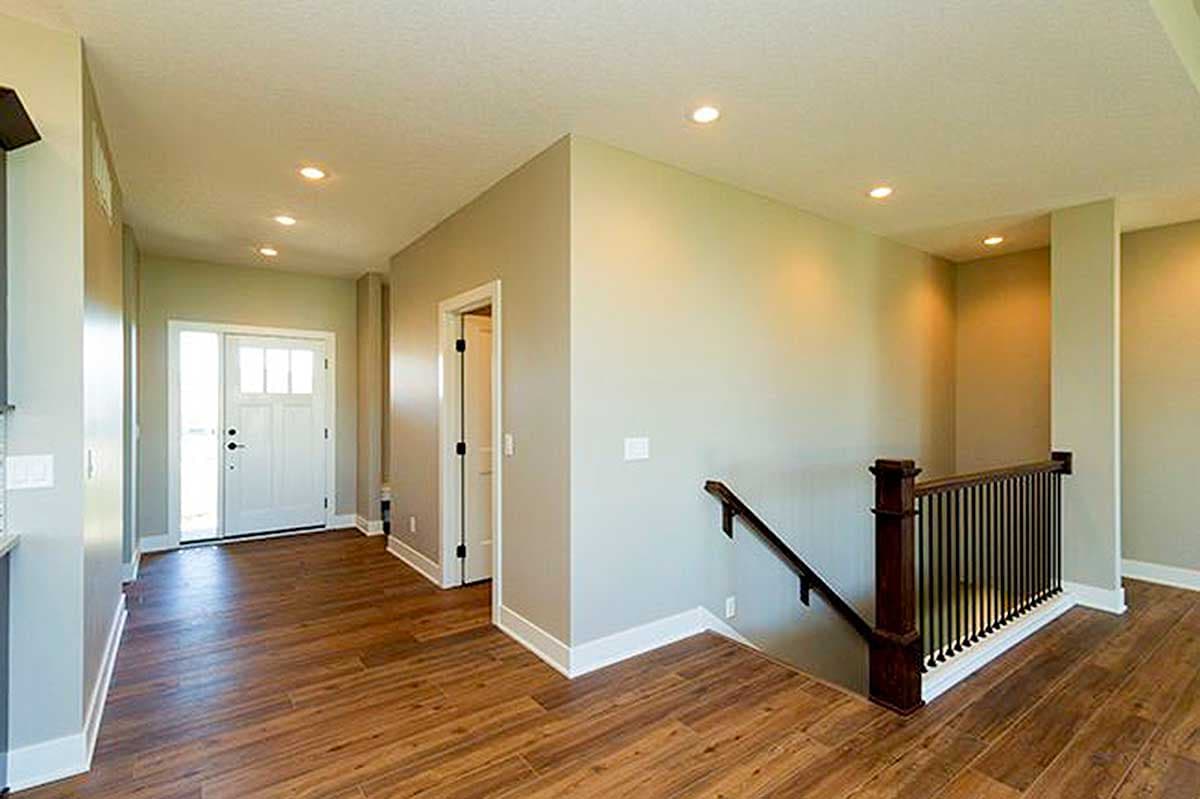Interior view of house entryway with wood floor, white front door with glass panes, and staircase with dark wood railing.