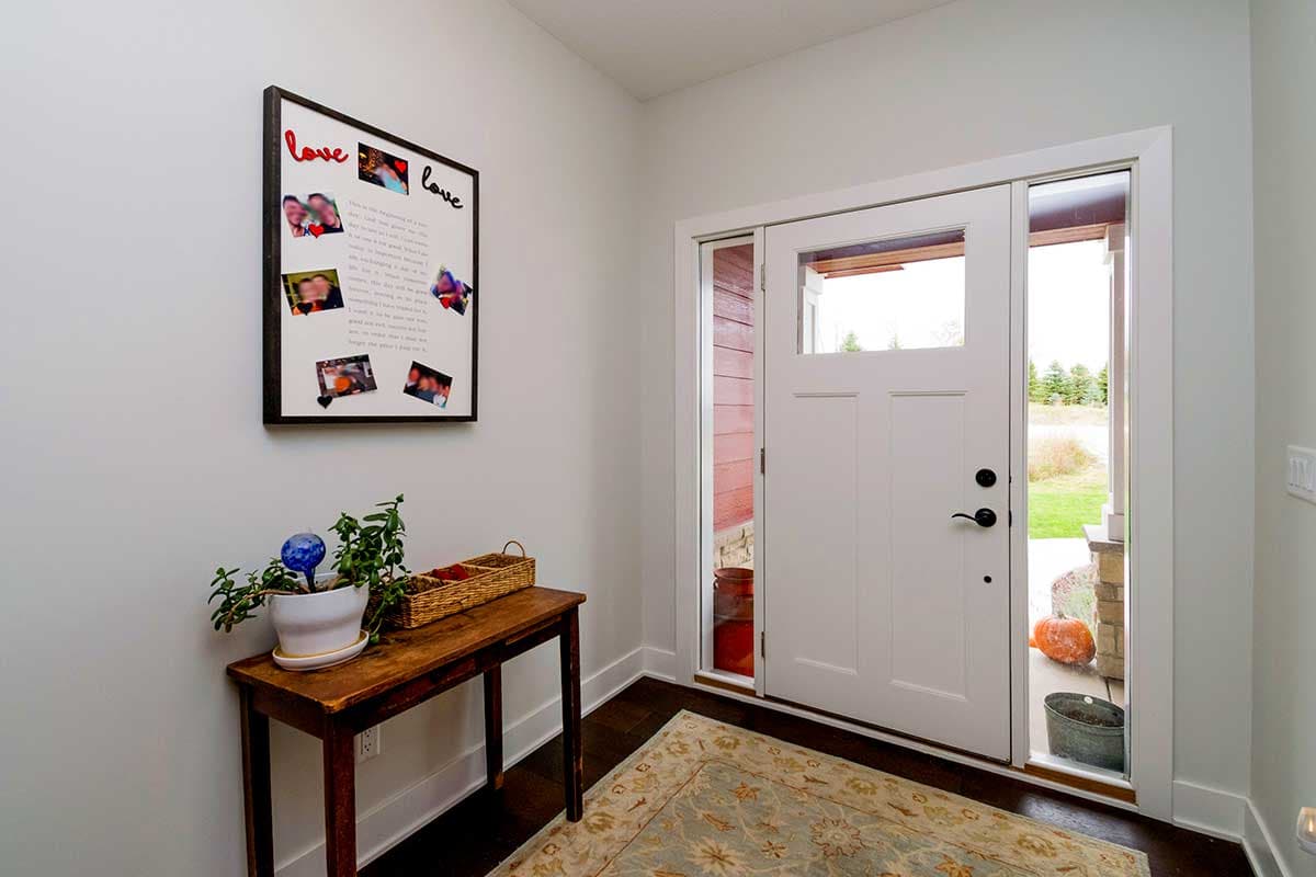 Entryway with a white paneled door, sidelight windows, framed photo collage on the wall, and console table.