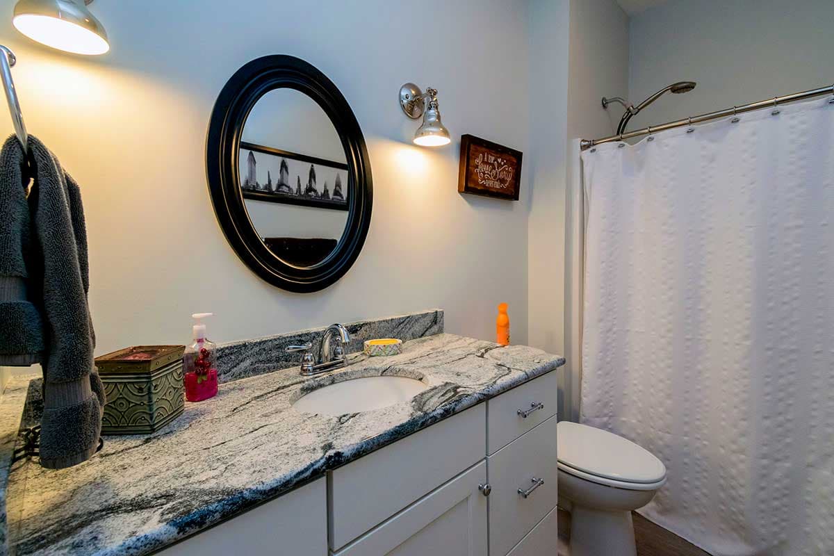 Bathroom with granite-top vanity, oval mirror, and shower with white textured curtain.