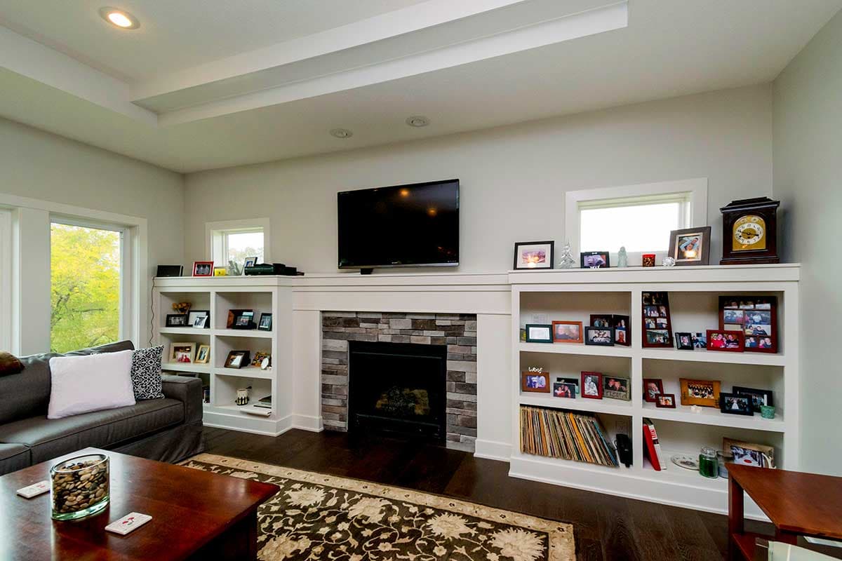 Living room with gas fireplace, built-in shelving, and coffered ceiling. A sofa and coffee table are visible.