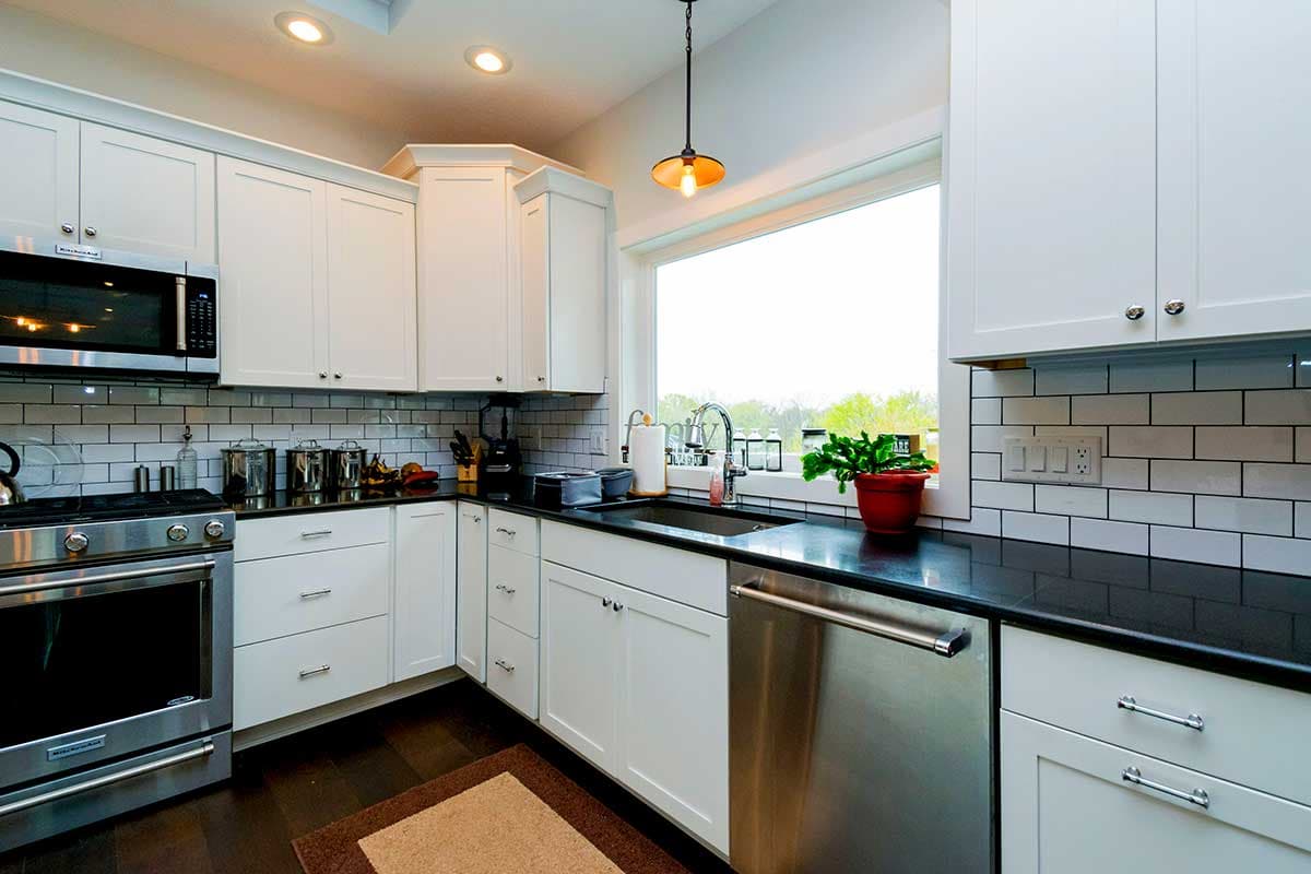 Kitchen with white shaker cabinets, stainless steel appliances, subway tile backsplash, and a large window over the sink.