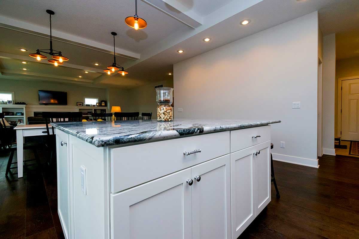 Kitchen island with granite countertop, shaker cabinets, and pendant lights. Open layout with dining and living area beyond.