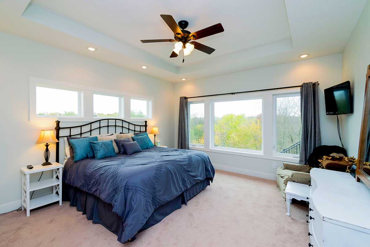 Primary bedroom with coffered ceiling, ceiling fan, and large windows overlooking trees.