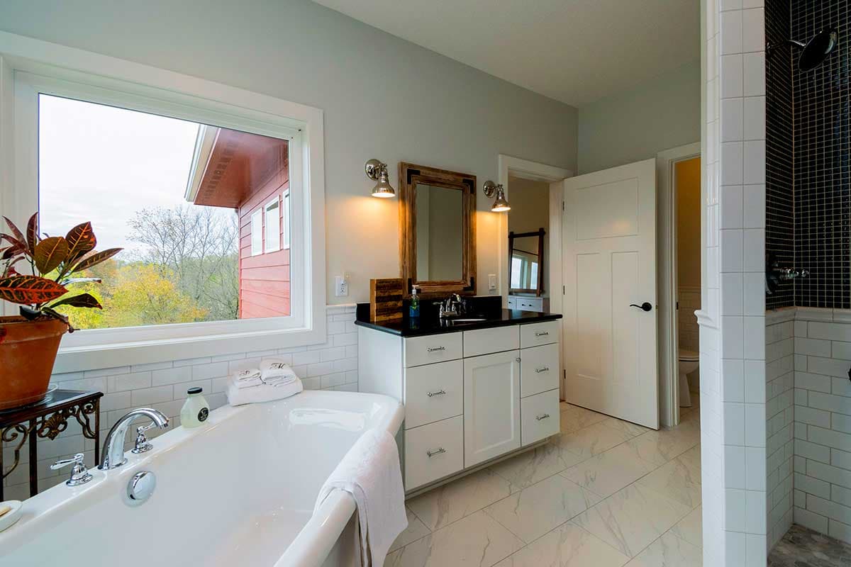 Bathroom featuring a freestanding tub, double vanity with black countertop, and a tiled shower with black mosaic accent.