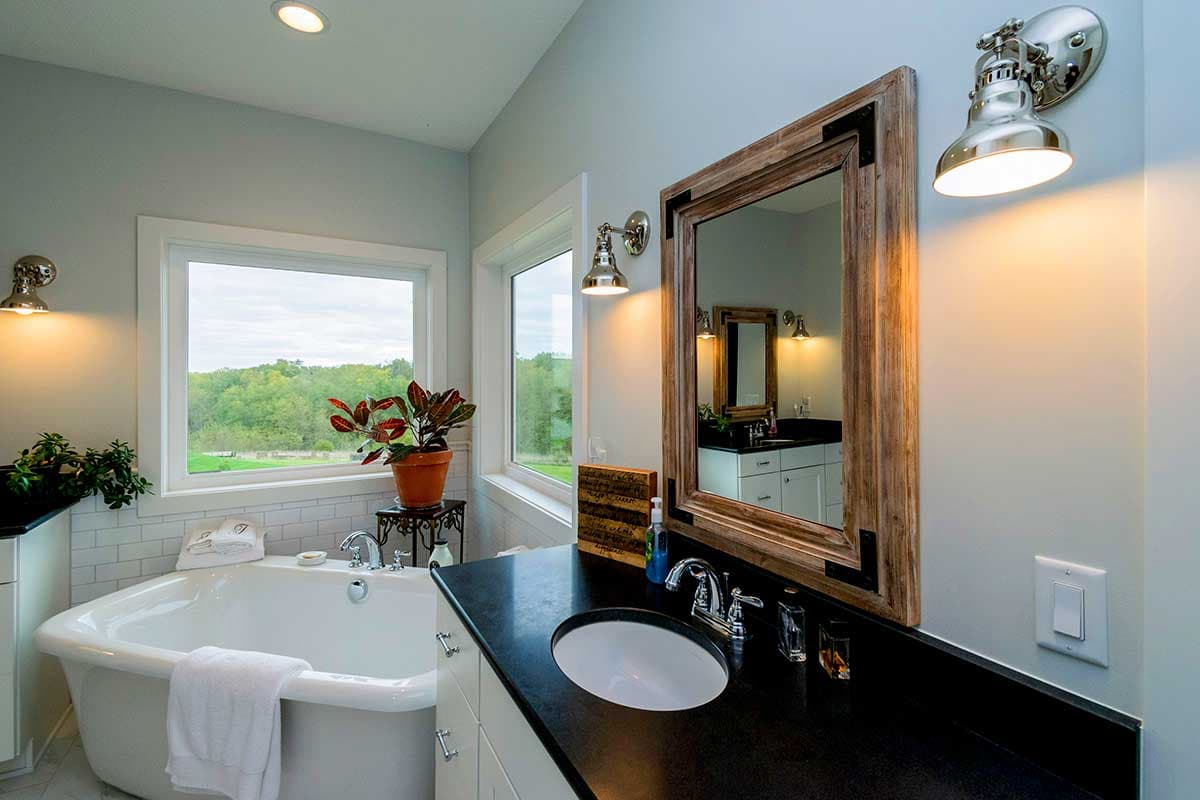 Bathroom interior with freestanding tub, double vanity, subway tile backsplash, and large windows overlooking landscape.