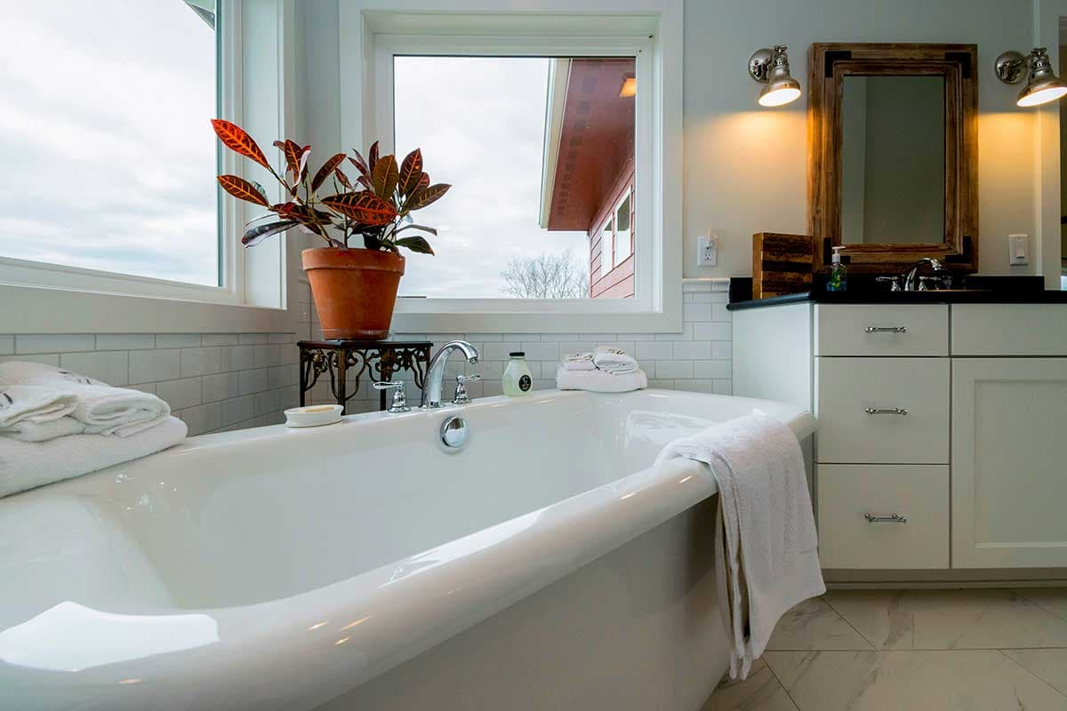 Freestanding bathtub with chrome fixtures, white subway tile backsplash, and white vanity with dark countertop.