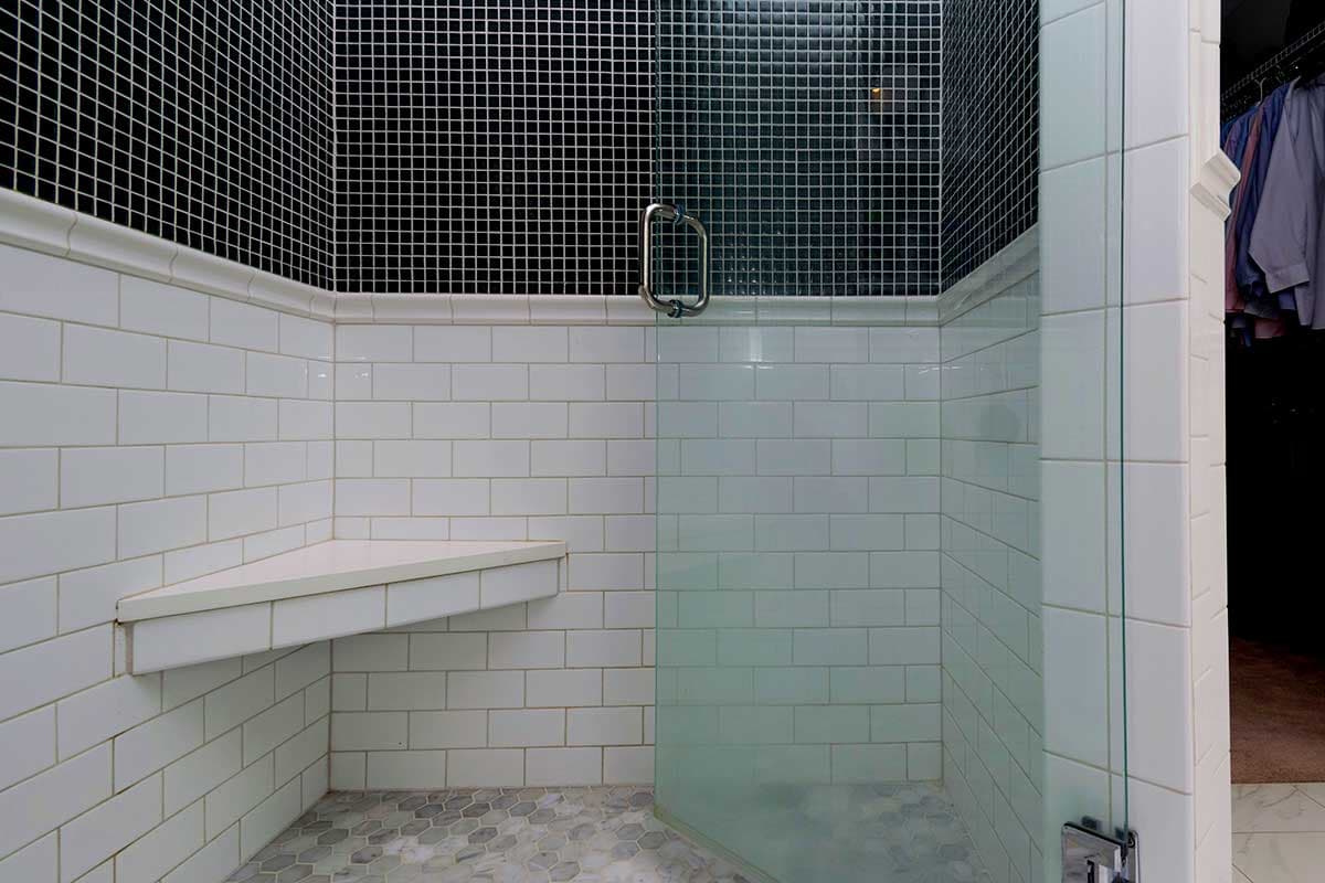 Shower with white subway tile, black mosaic tile accent, corner bench, and glass enclosure.