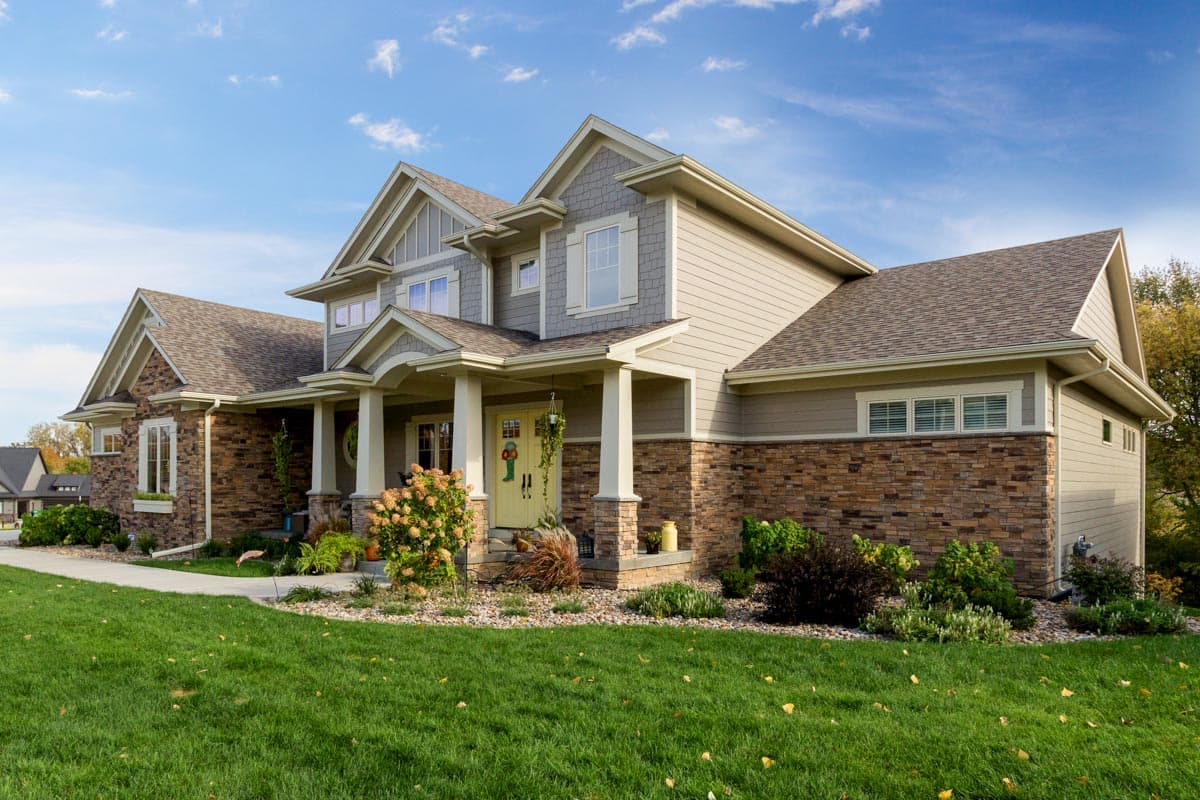 House plan exterior: two-story home with a covered front porch, gabled dormers, and stone accent siding.