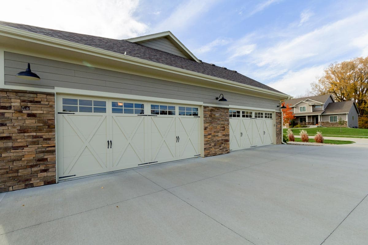 House plan exterior: Three-car garage with stone accents, paneled doors with X-design, and overhead windows.